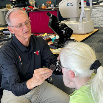 Dr. R. Tracy Williams is helping a young student with her glasses