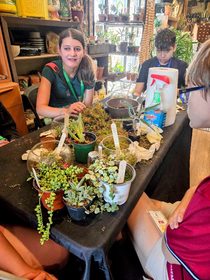 A Trip to Cosley Zoo with Grandma Martyl's Low Vision Day Camp 23 two young people talk aver a table of potted plants.