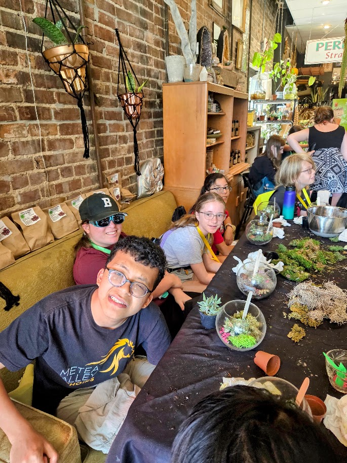 A Trip to Cosley Zoo with Grandma Martyl's Low Vision Day Camp 27 a group of campers posing while sitting at a table full of potted plants.