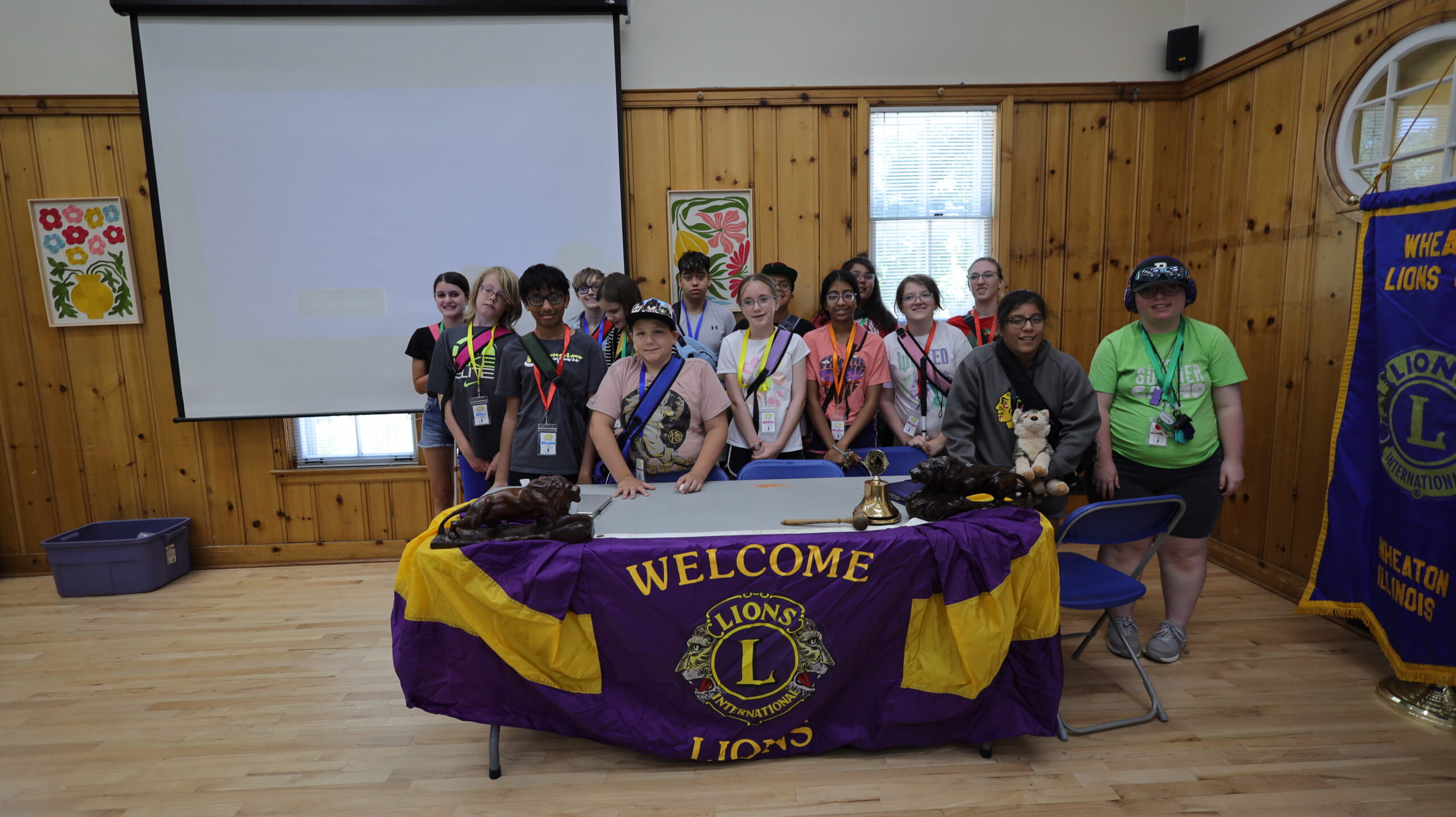 group of teenagers stand behind table with a Wheaton Lions welcome banner.