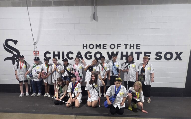 A Trip to Cosley Zoo with Grandma Martyl's Low Vision Day Camp 36 group of campers pose in front of a wall that says Home of the Chicago White Sox