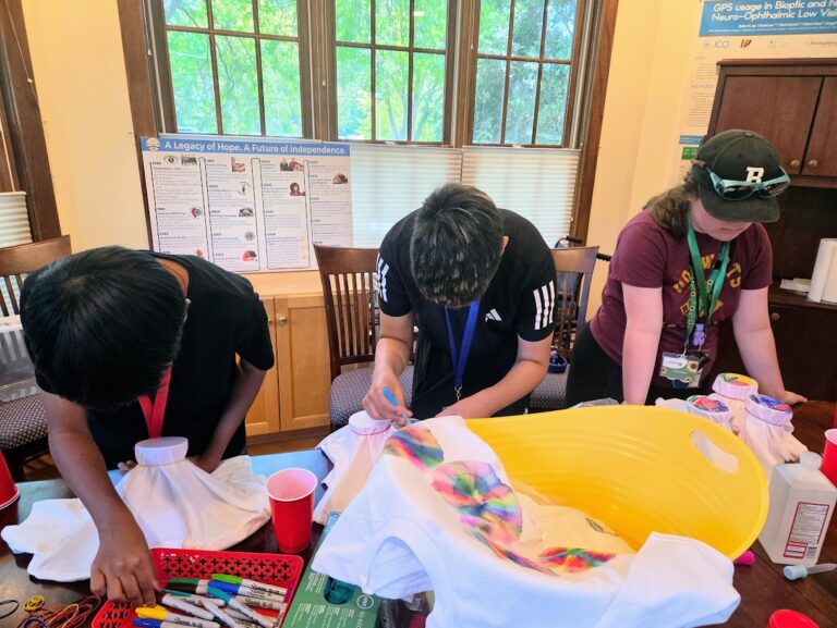 A Trip to Cosley Zoo with Grandma Martyl's Low Vision Day Camp 30 three people hunched over a table to work on a tie dye project.